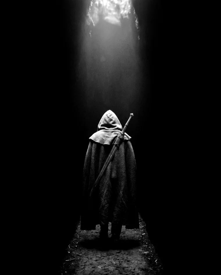 A hooded figure walking away down a shaft of light